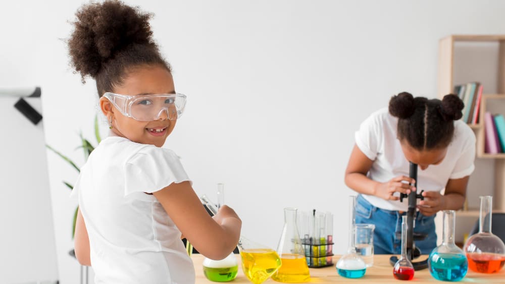 Duas meninas usando vidraria e reagentes de laboratório.