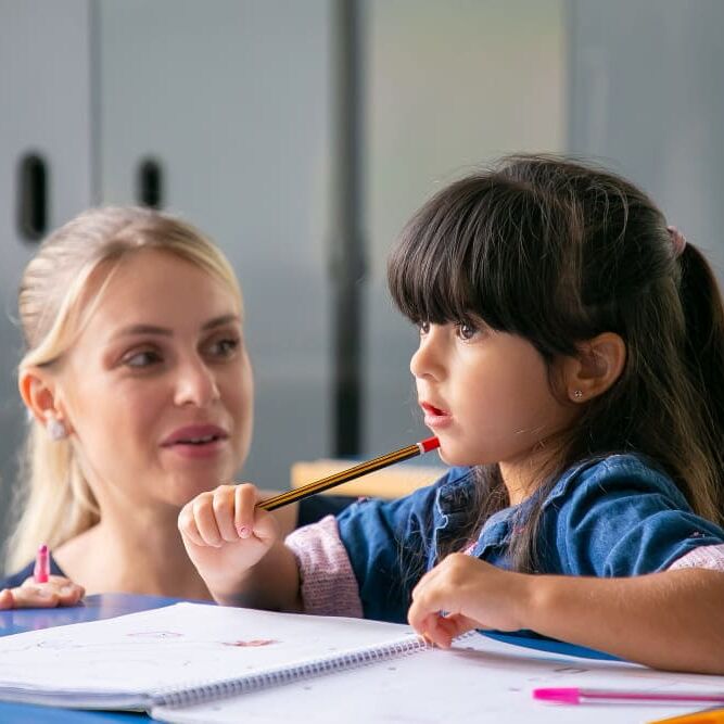cheerful-young-school-teacher-helping-little-schoolgirl-to-do-her-task (1) (1) cheerful-young-school-teacher-helping-little-schoolgirl-to-do-her-task (1) (1)